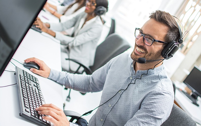 life insurance agent at office wearing phone headset smiling at computer screen because he sells bigger policies