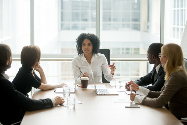 Female Insurance Agency Owner Sitting with Team at Table Leading Conversation